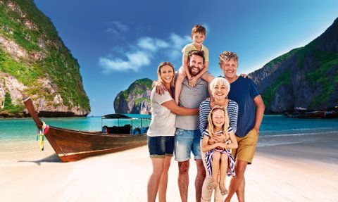 Eine fröhliche Familie posiert am Strand, umgeben von beeindruckenden Klippen und einem Boot im Hintergrund.
