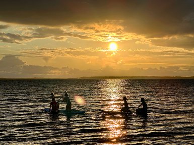 Silhouetten von Menschen, die auf Stand-Up-Paddle-Boards im Sonnenuntergang paddeln, während das Wasser glitzert.