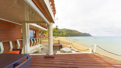 Ein Blick auf einen Strand mit sanften Wellen, umgeben von üppigem Grün und einem einladenden Holzdeck im Vordergrund.