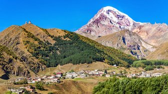 Die majestätischen Berge umgeben ein malerisches Dorf, während der schneebedeckte Gipfel im Hintergrund strahlt.