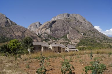 Eine ländliche Szene mit traditionellen Häusern, umgeben von sanften Hügeln und majestätischen Felsen unter klarem Himmel.