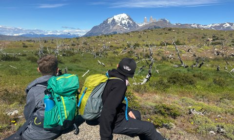 Zwei Kinder sitzen auf einem Felsen und blicken auf die beeindruckenden Torres del Paine in der Ferne.
