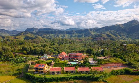 Eine malerische Ansicht des Ranomafana Hotels, umgeben von üppigen grünen Hügeln und Reisfeldern unter einem blauen Himmel.