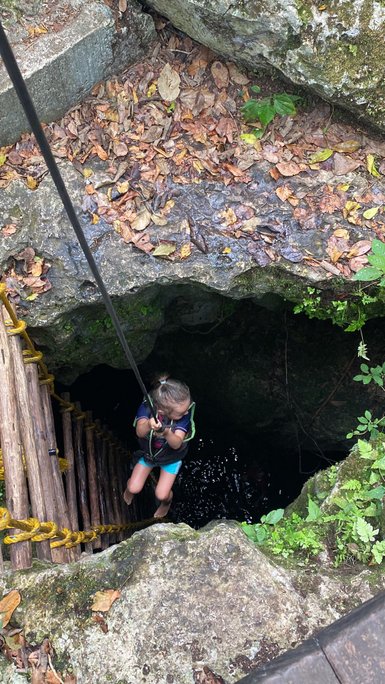 Ein Kind steigt vorsichtig über eine steile Holzleiter in eine dunkle Höhle im Punta Laguna Park hinab – Mexiko Familienreise