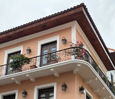Ein elegantes, zweistöckiges Gebäude mit einem schönen, verzierten Balkon und blühenden Pflanzen in Töpfen.
