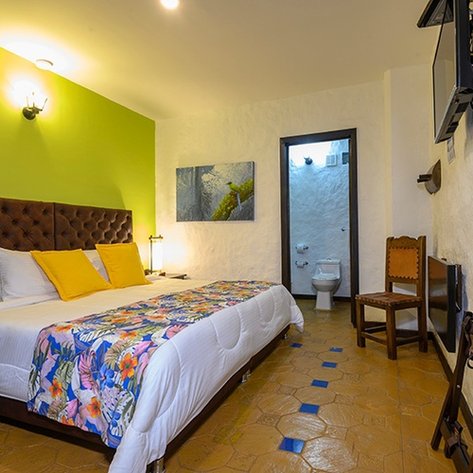 Ein gemütliches Hotelzimmer mit einem großen Bett, bunten Kissen und einem lebhaften grünen Akzent an der Wand.