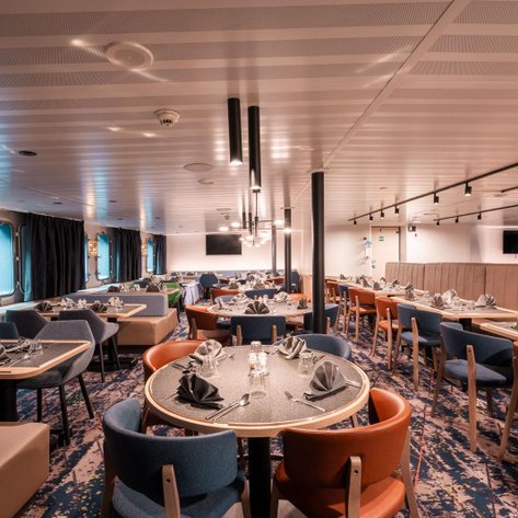 Ein elegantes Restaurant mit runden Tischen, stilvollen Stühlen und einer modernen Innenausstattung auf einem Schiff.