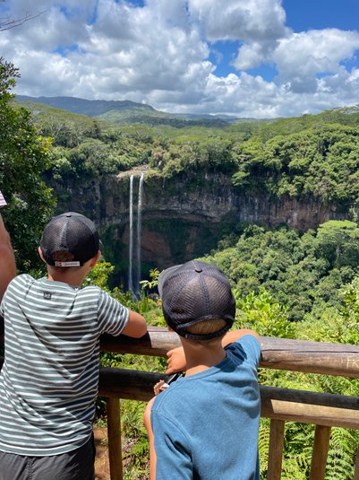Zwei Kinder stehen an einem Geländer und blicken auf den beeindruckenden Chamarel-Wasserfall in Mauritius.