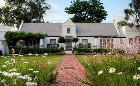 Ein charmantes Cottage mit einem begrünten Garten, umgeben von bunten Blumen und einem gepflasterten Weg.