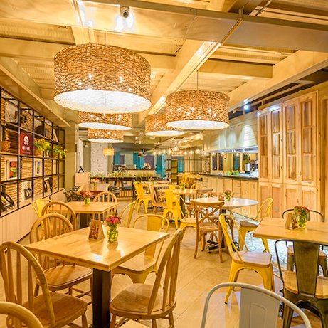 Ein modernes Restaurant mit warmem Licht, Holztischen und bunten Stühlen, das eine einladende Atmosphäre schafft.