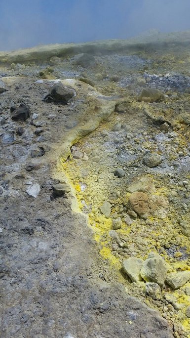 Eine vulkanische Landschaft mit gelben und grauen Mineralien, die sich über einen steinigen Boden erstrecken.