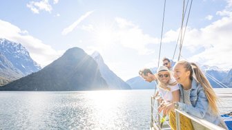 Fünf fröhliche Menschen genießen die Aussicht auf Milford Sound, während sie auf einem Boot in der Sonne stehen.