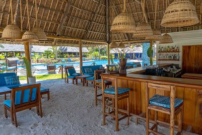 Ein einladender Barbereich mit Holzstühlen und blauen Kissen, umgeben von einem tropischen Pool und üppiger Vegetation.