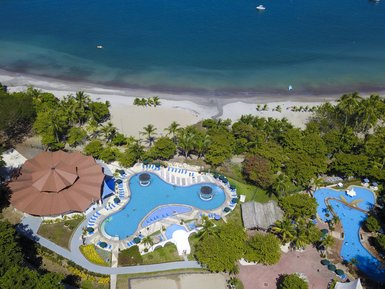 Ein atemberaubender Blick auf einen Poolbereich umgeben von üppigem Grün und dem blauen Ozean im Hintergrund.