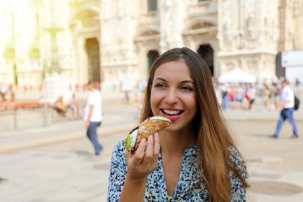 Eine junge Frau genießt einen Cannolo in einer belebten Stadtstraße, umgeben von historischen Gebäuden und Passanten.