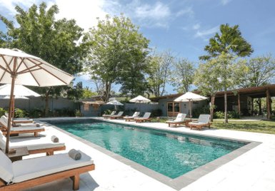 Ein einladender Poolbereich mit Liegen und Sonnenschirmen, umgeben von üppigem Grün und strahlend blauem Himmel.