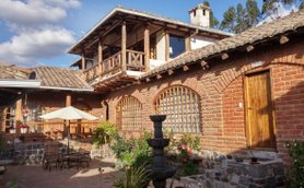 Eine charmante Hacienda mit roten Ziegelwänden, einem Innenhof und einem Brunnen, umgeben von Pflanzen und Blumen.