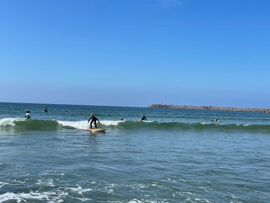 Surfer reitet auf einer Welle, während andere Surfer im Hintergrund im Wasser paddeln und die Sonne scheint.