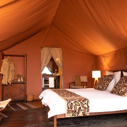 Ein gemütlicher Schlafbereich in einem Zelt mit einem großen Bett und warmen, erdigen Farbtönen, die eine einladende Atmosphäre schaffen.