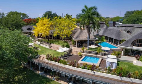 Eine weitläufige Hotelanlage mit einem Pool, umgeben von üppigem Grün und bunten Blumen, strahlt tropisches Flair aus.