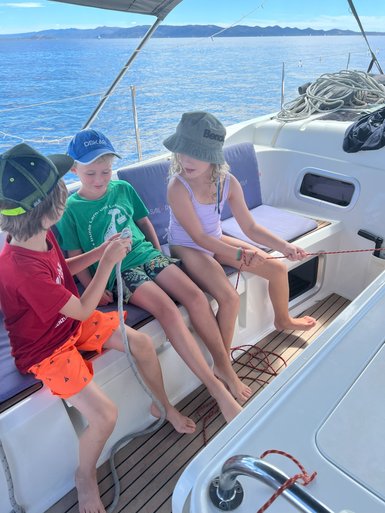 Drei Kinder sitzen auf einem Boot und lernen, wie man mit einem Seil umgeht, während sie den Ozean genießen.