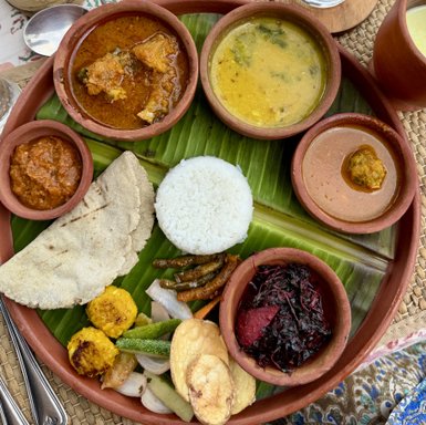 Ein traditionelles indisches Essen auf einem Teller aus Ton, serviert mit Reis, verschiedenen Currys und frischem Gemüse.