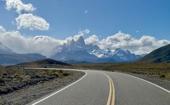 Eine kurvenreiche Straße führt durch eine atemberaubende Landschaft mit schneebedeckten Bergen im Hintergrund.