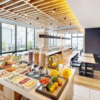 Ein modernes Restaurant mit großen Fenstern, das eine Vielzahl von frischen Speisen und Getränken auf einem Buffet präsentiert.