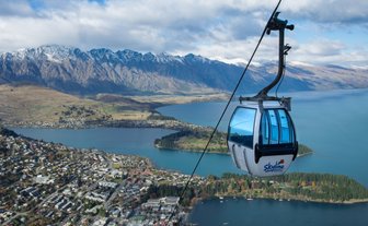 Eine Gondel schwebt über die malerische Landschaft von Queenstown, umgeben von majestätischen Bergen und glitzerndem Wasser.