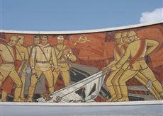 Ein Wandgemälde zeigt Soldaten, die gemeinsam ein Symbol des Widerstands aus dem Boden ziehen, umgeben von historischen Elementen.