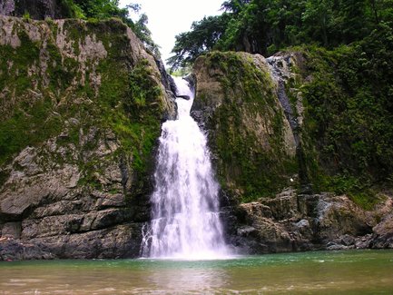 Ein majestätischer Wasserfall stürzt über grüne Felsen in einen klaren, ruhigen Pool, umgeben von üppiger Vegetation.