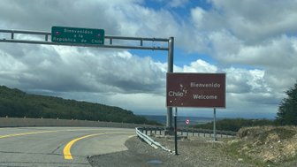 Ein Willkommensschild an der Grenze zu Chile, umgeben von grünen Hügeln und einem bewölkten Himmel.