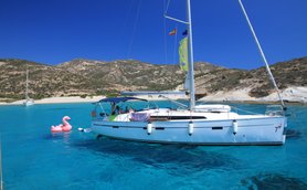 Ein Segelboot schaukelt sanft auf dem klaren, blauen Wasser, während ein pinker Flamingo-Schwimmring daneben schwimmt.
