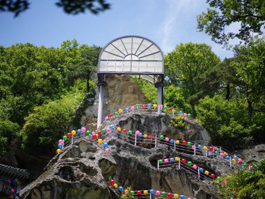 Eine bunte Treppe aus Ballons führt zu einer beeindruckenden Felsformation, die von üppigem Grün umgeben ist.