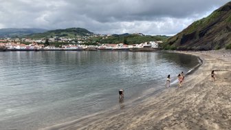 An einem ruhigen Strand spielen Kinder im flachen Wasser, während die sanften Wellen sanft an den Sandstrand plätschern.