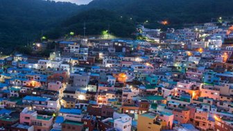 Die bunten Häuser des Gamcheon Culture Village leuchten in der Dämmerung, umgeben von sanften Hügeln und einem klaren Himmel.