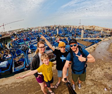 Familie macht Selfie vor blauen Fischerbooten im Hafen von Essaouira – Marokko Familienreise