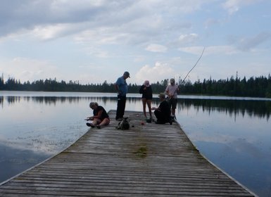 Eine Gruppe von fünf Personen steht und sitzt auf einem Holzsteg, während sie am Wasser angeln und entspannen.