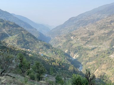 Eine atemberaubende Berglandschaft in Nepal mit sanften Hügeln und terrassierten Feldern, die in der Ferne verschwommen sind.