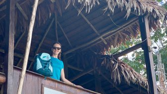 Eine Frau steht auf einem Balkon des Heliconia Amazon River Lodge in Peru, lächelnd mit einem Rucksack auf der Schulter.