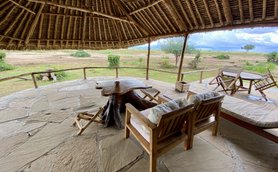 Eine gemütliche Terrasse mit Holzstühlen und einem Tisch aus Baumstamm, umgeben von einer weiten, grünen Landschaft.