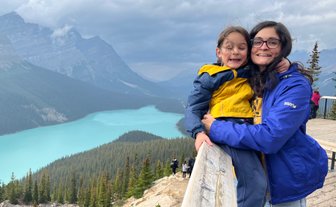 Eine Frau umarmt ein lächelndes Kind an einem Aussichtspunkt mit Blick auf den türkisfarbenen Peyto Lake und die umliegenden Berge.