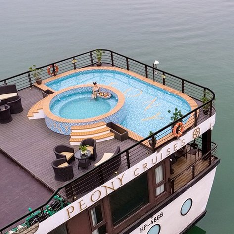Ein luxuriöser Pool auf dem Deck eines Kreuzfahrtschiffes, umgeben von stilvollen Sitzgelegenheiten und Pflanzen.