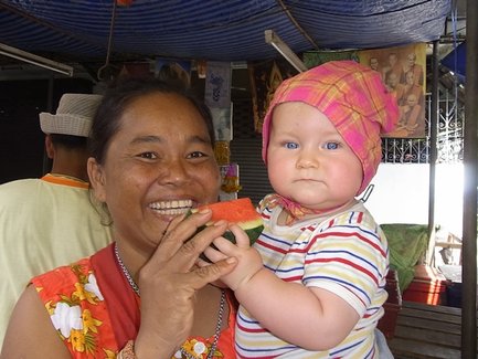 Eine fröhliche Frau hält ein Stück Wassermelone, während sie ein Baby mit blauen Augen in den Armen hält.