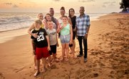 Eine Gruppe von acht Personen steht am Strand, umgeben von sanften Wellen und einem farbenfrohen Sonnenuntergang.