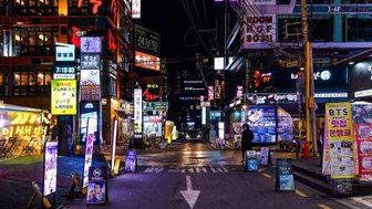 Eine belebte Straße in Gangnam, beleuchtet von bunten Neonlichtern und Werbetafeln, die das nächtliche Stadtleben zeigen.