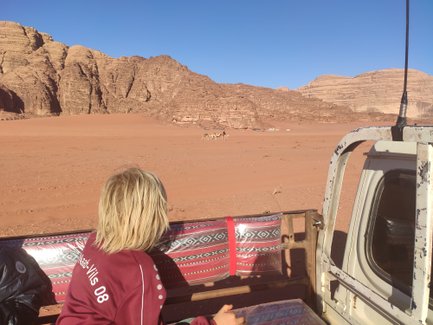 Ein Kind mit blonden Haaren sitzt in einem Jeep und blickt auf die beeindruckenden Felsen von Wadi Rum.