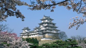 Das majestätische Himeji-Schloss erhebt sich über blühende Kirschbäume und strahlt im klaren blauen Himmel.