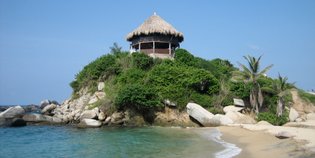 Ein malerisches Strandhaus mit Strohdach thront auf einer bewachsenen Klippe, umgeben von klarem Wasser und sanften Wellen.