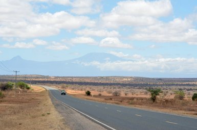 Eine kurvenreiche Straße führt durch eine trockene Landschaft, mit einem Fahrzeug, das in der Ferne fährt.